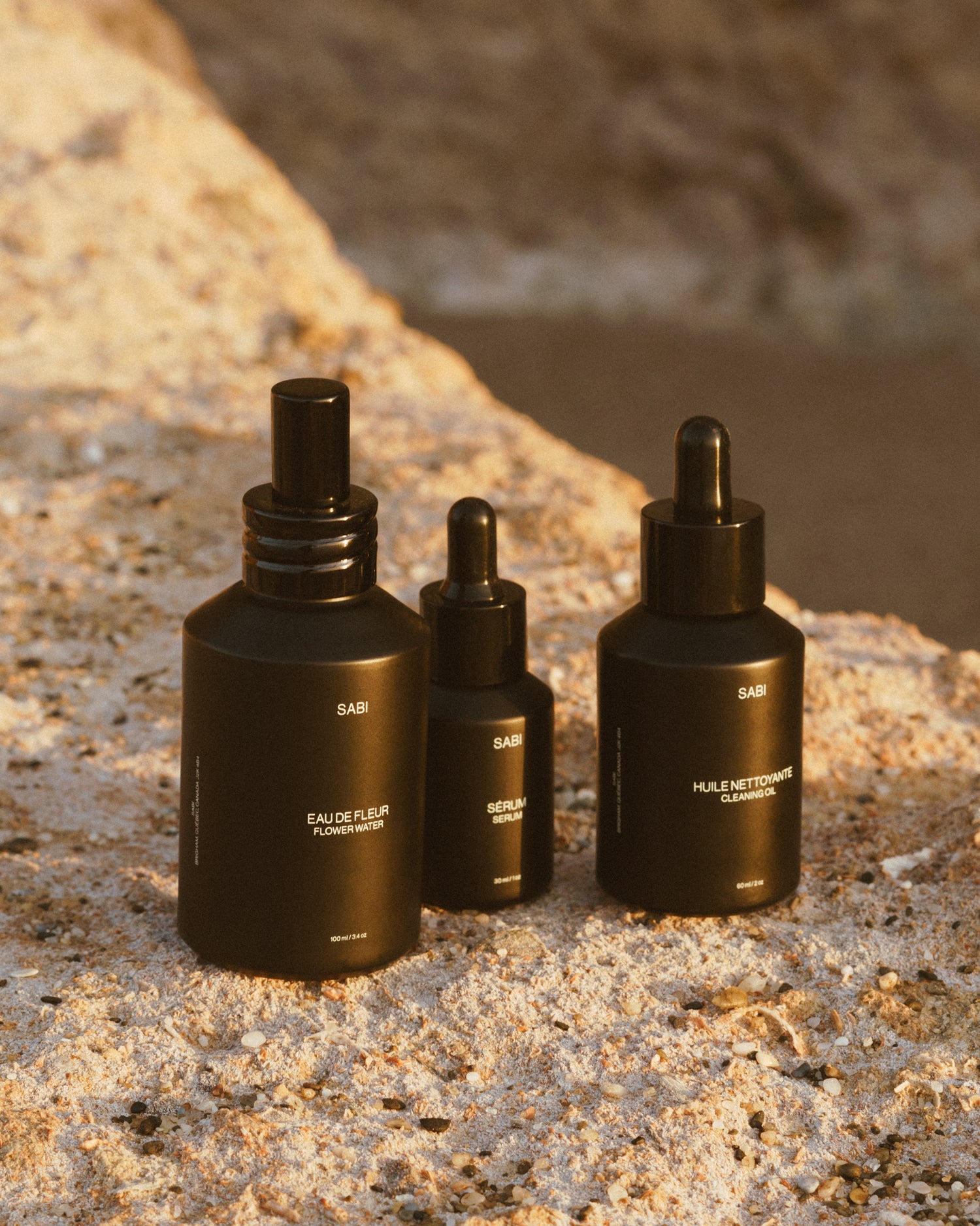 Three black skincare bottles labeled 'SABI' on a textured stone surface.