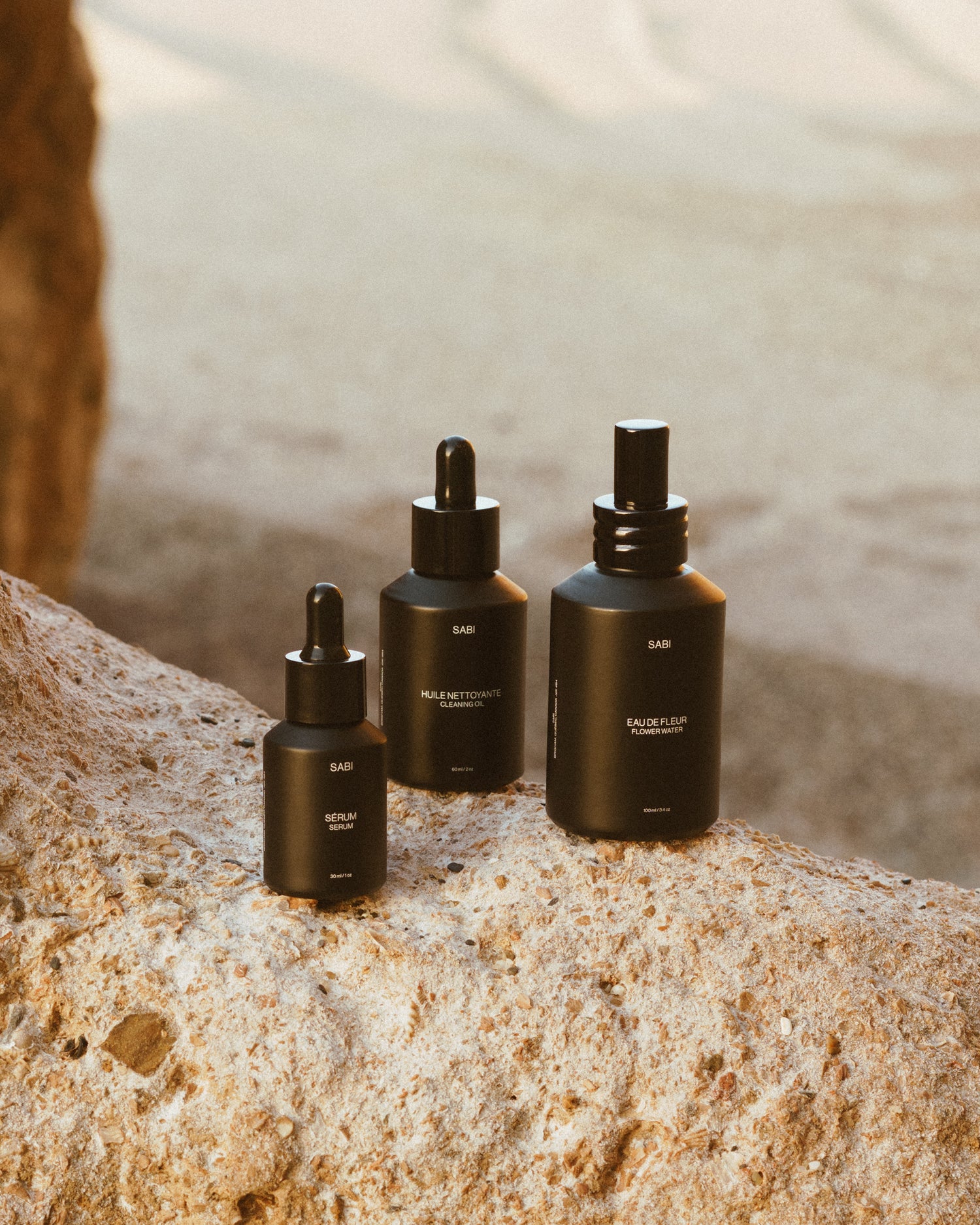 Three black dropper bottles on a rock with a blurred natural background