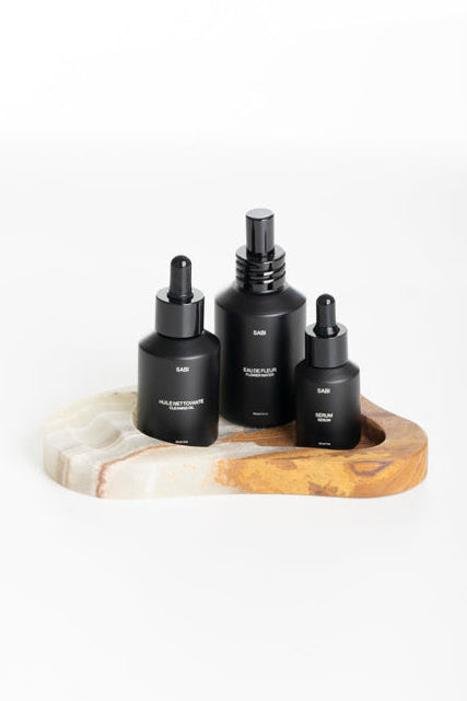 Three black bottles with droppers on an onyx stone tray against a white background