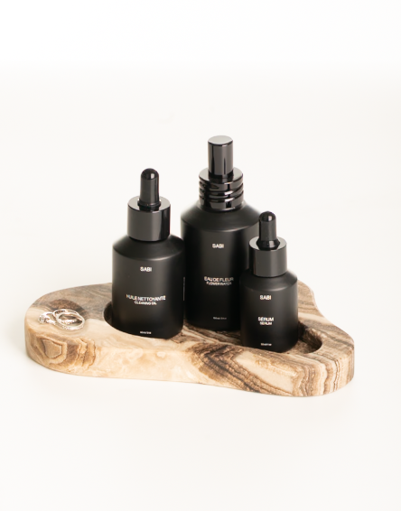 Three black bottles with droppers on a wooden stand against a white background