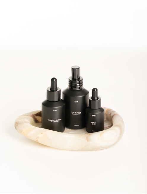 Three black bottles with droppers on a marble tray against a white background